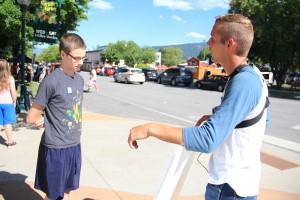 Abolitionist Chris Hutto, right, shows a large sign depicting a dismembered foot from an aborted fetus to a young Farmers’ Market attendee last week at Farmin Park. Photo by Ben Olson.