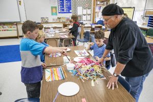 Tom Callister, right, looks on as Owen Hughes, left, Paul Kent, behind, Kai Longanecker, right, glue strips of tissue in various designs in Jenny Smith’s third grade Washington Elementary School class on Friday. Photo by Cameron Barnes.