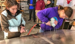 Aerospace students Caleb Watson, left, and Anne Watson, right, install replacement rivets into wing of Zenith Zodiac during plane-building project in  Sandpoint airport hangar.